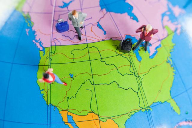 Miniature figures of travelers with luggage standing on a colorful world map, representing the concept of global travel and exploration. Ideal for use in travel blogs, tourism advertisements, educational materials, and articles about international travel planning.