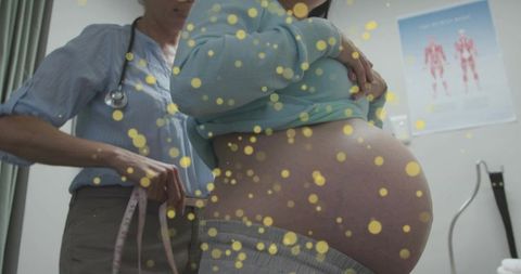 Clinician measuring pregnant belly with tape during prenatal visit with warm bokeh lights