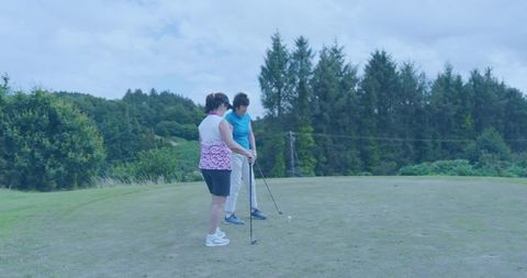 Women practicing golf on tee sharing instruction and teamwork on lush overcast course