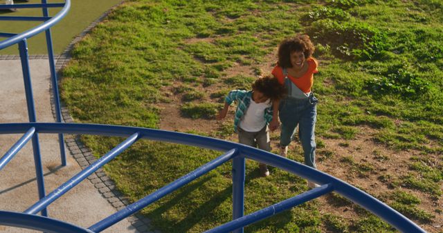 Happy biracial mother and son holding hands walking at sunny playground, copy space. Motherhood, childhood, summer, vacations, fun and free time, unaltered.