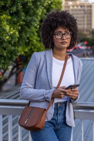 Young african american woman standing on urban bridge using smartphone at dusk
