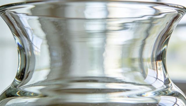 Backlit flared glass vessel bending light with soft bokeh and translucent reflections