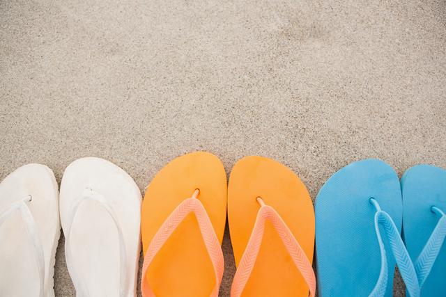 Brightly colored flip flops neatly arranged in a row on sandy beach. Ideal for travel brochures, summer promotions, beach party invitations, and vacation websites.
