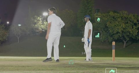 Batsman and bowler standing on night cricket pitch displaying augmented reality stats