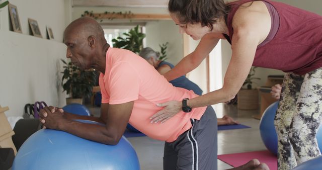 Physical therapy session featuring a senior man receiving assistance during an exercise routine with an exercise ball. Ideal for depicting healthcare, physiotherapy, rehabilitation and senior well-being. Can be used in articles, advertisements and promotional content for fitness, health care services and senior wellness programs.