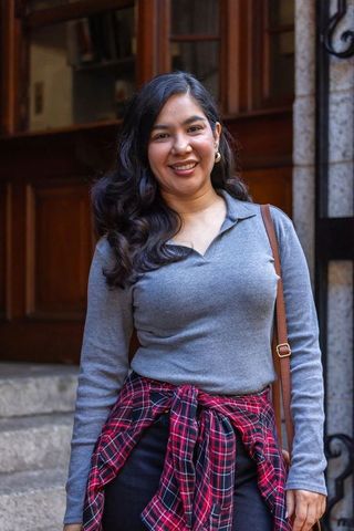 Smiling woman on city steps wearing gray sweater and red plaid shirt tied at waist