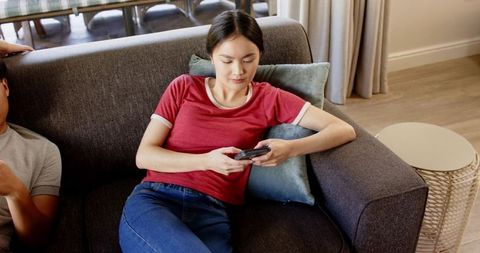 Young Woman Seated on Sofa Using Smartphone in Relaxed Setting
