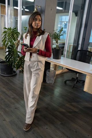 Indian professional standing in open-plan office holding smartphone wearing smartwatch