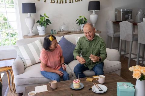 Asian senior couple celebrating birthday at home placing candles on mini cake