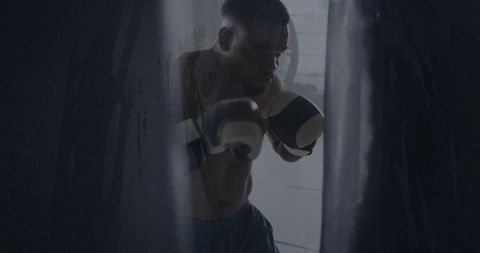 Determined Boxer Training with Heavy Bag in Dimly Lit Gym