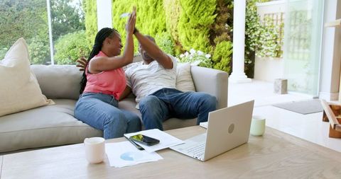 Joyful Couple Celebrating Success at Home with Laptop and Documents