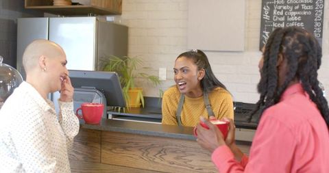 Indian barista serving two customers at wood counter, friendly coffee shop interaction