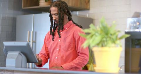 African american barista operating touchscreen pos at cafe counter with yellow plant