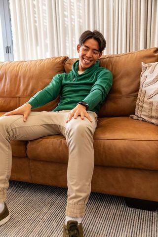 Asian man relaxing on leather couch smiling wearing green pullover and smartwatch
