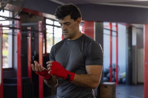 Man wrapping hands with red wraps in gym preparing for boxing training and workout