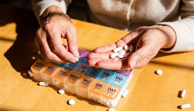 Senior Hands Organizing Daily Medication in Weekly Pill Organizer on Wooden Table