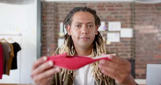 Portrait of biracial male designer with dreadlocks holding red shoe at office. Business, design, fashion and work, unaltered.