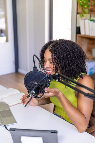 African american woman podcasting from home office with professional microphone and laptop