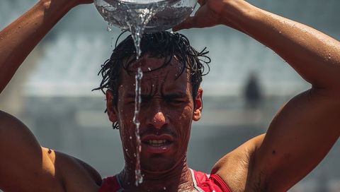 Athlete pouring water over head from metal bowl during intense sun-drenched track session