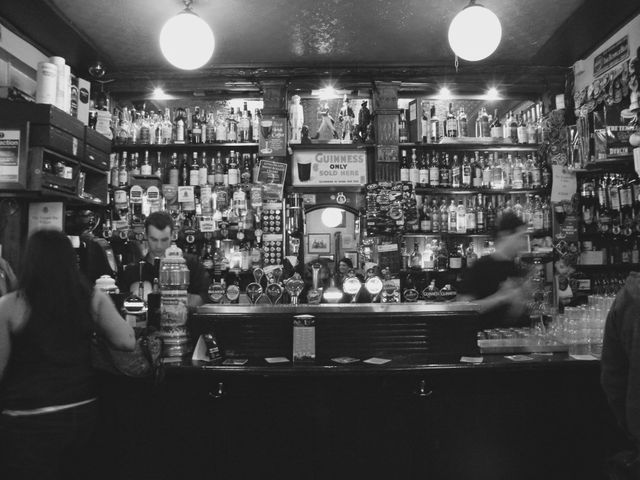 People enjoying an evening at a busy Irish pub. Heavily stocked bar with various liquors and a welcoming atmosphere. Suitable for illustrations of nightlife, drinking culture, social gatherings, and vintage pubs.