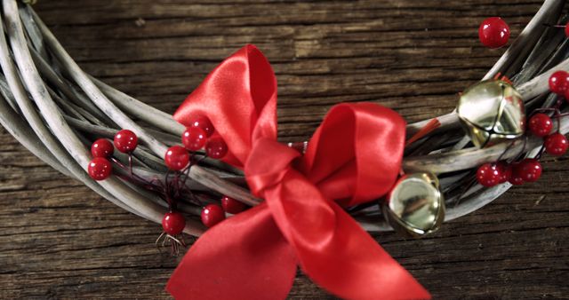 A festive wreath adorned with a bright red bow, red berries, and small bells rests on a wooden surface, symbolizing holiday cheer. Its rustic charm evokes the warmth of traditional Christmas decorations.