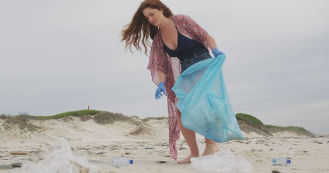 Caucasian woman wearing latex gloves collecting rubbish from the beach looking ahead. ecology beach conservation volunteer.