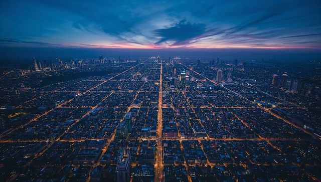 Dramatic aerial city grid at dusk with glowing central boulevard leading to skyline