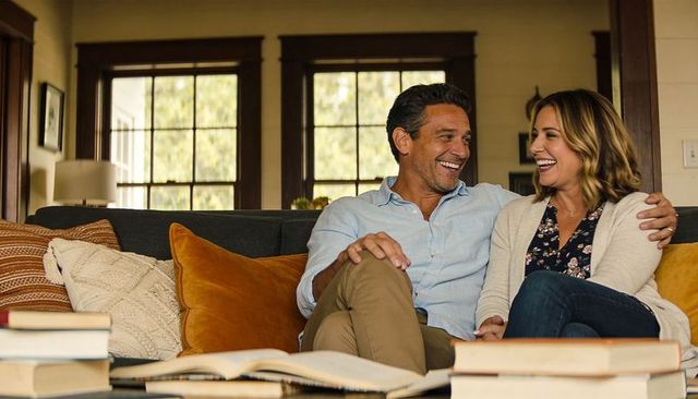 Smiling couple cuddling on dark sofa in cozy craftsman living room with books