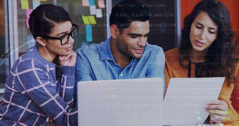 Collaborative team reviewing analytics on laptop and documents in modern coworking space