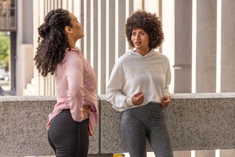 Diverse women chatting after workout on urban balcony wearing hoodies and leggings