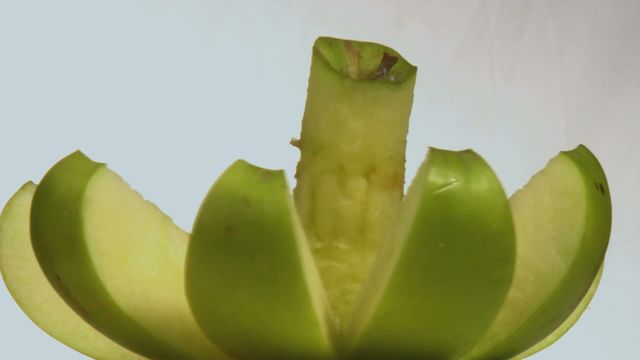 This image presents a close-up view of a sliced green apple, using a technique that displays each slice while keeping the core intact. The style emphasizes freshness and creativity in food presentation, making it suitable for culinary blog posts, healthy eating campaigns, or recipe illustrations. It can also be used in kitchen design brochures or product packaging for food products.