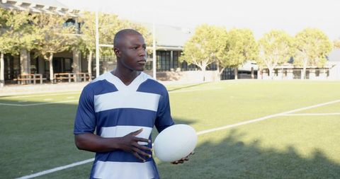 Rugby player holding ball on sunlit pitch wearing striped jersey preparing for play