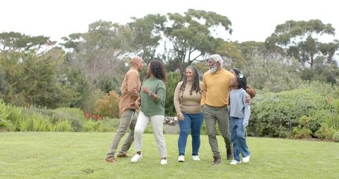 Multigenerational family walking together on park lawn laughing and embracing outdoors