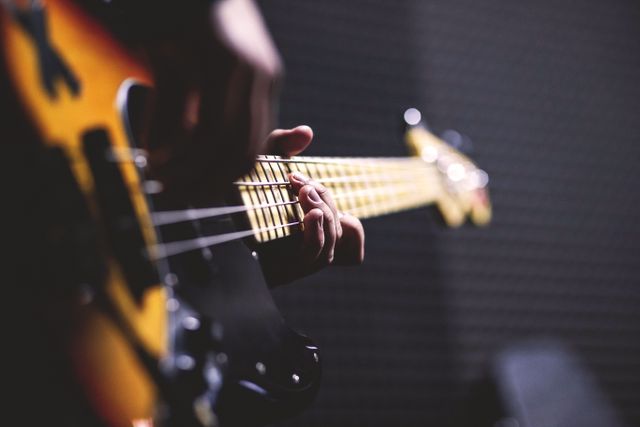 Close-up view of a musician's hand playing an electric bass guitar, focusing on the strings and frets. Perfect for illustrating musical passion, live performances, band practice, or educational content related to learning and mastering musical instruments. Great for use in blogs, articles, advertisements, and social media posts about music and musicianship.