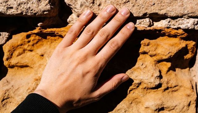Pressing hand against sunlit weathered rock showing texture, veins, skin detail