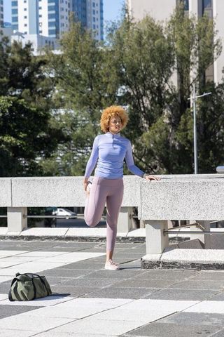 African american woman stretching on rooftop in pastel athleisure urban fitness training