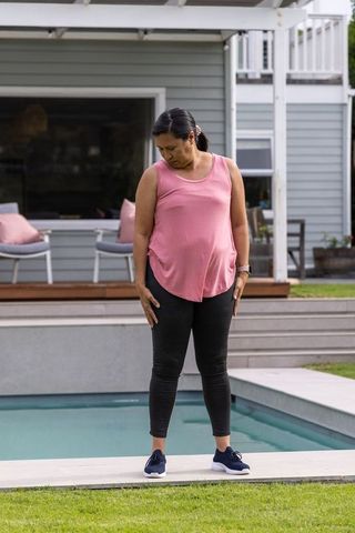 Mature woman checking smartwatch at poolside backyard in pink tank top and leggings