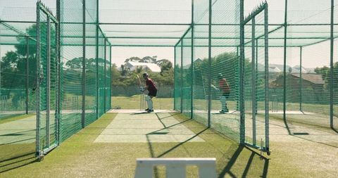 Indian cricketer practicing batting in outdoor nets with bowler during training session