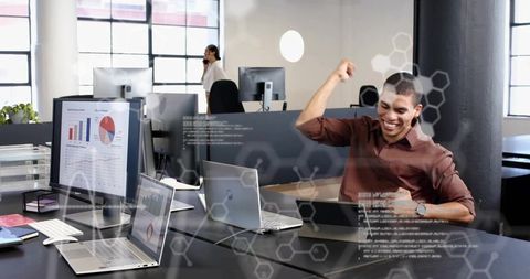 Man celebrating success at laptop in modern open-plan office with analytics charts