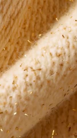 Slow panning macro over cream wool knit threaded with metallic gold flecks