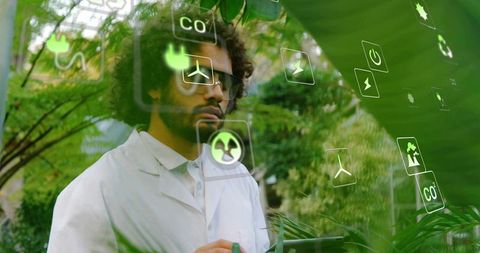 Greenhouse researcher using tablet and holographic eco icons while inspecting tropical plants