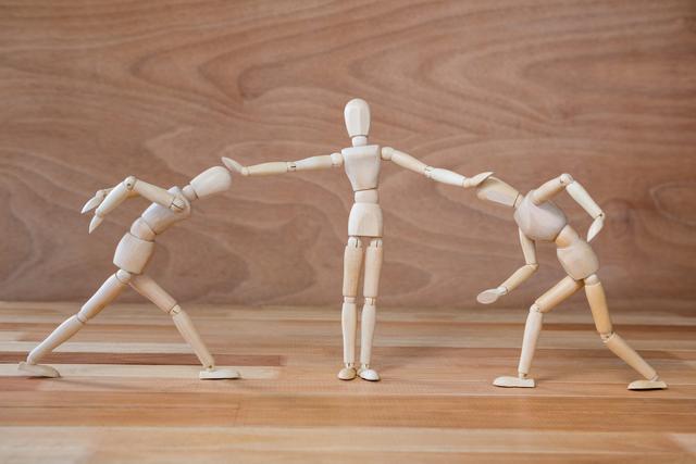 Wooden figurines depicting a referee stopping a fight between two others. Useful for illustrating concepts of conflict resolution, teamwork, mediation, and balance. Ideal for educational materials, presentations on conflict management, and creative projects.