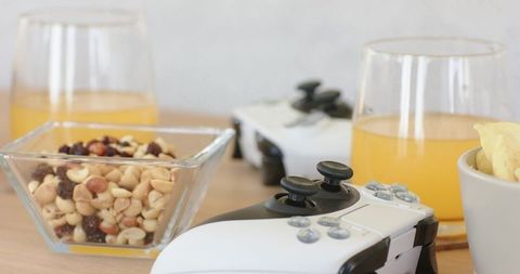 Casual gaming night snack setup with white black wireless controller, mixed nuts, drinks