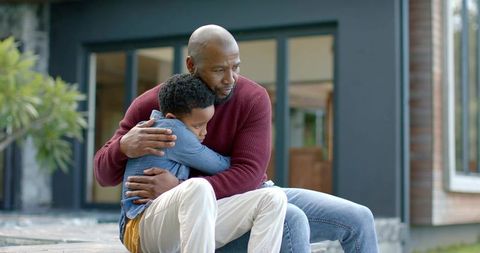 African american father hugging son on modern porch steps showing comfort and protection