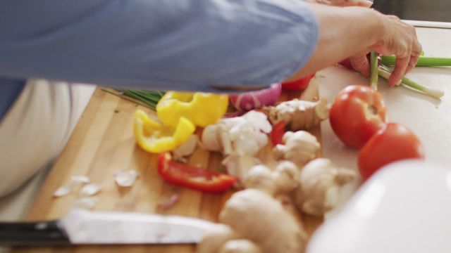 Close-up of an African American senior woman chopping vegetables including tomatoes, peppers, green onions, and garlic in a home kitchen. Useful for content related to healthy eating habits, retirement lifestyle, elderly activity, home cooking, and nutrition. Ideal for promoting senior living, culinary arts, or food preparation topics.