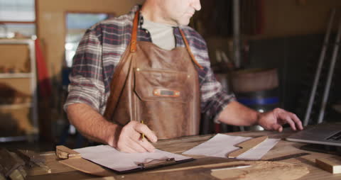 Craftsman Designing Knife in Workshop with Clipboard and Laptop