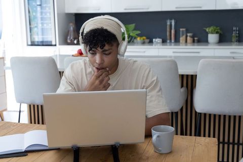 Black man working from home at kitchen table with beanie and headphones