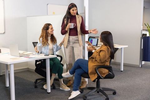 Multicultural female team collaborating over coffee in modern open-plan office workspace