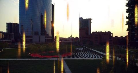 Sunset reflections over urban park amphitheater featuring curved glass towers and red circular lawn