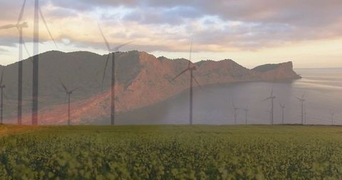 Golden meadow leading to coastal wind farm at sunrise with rugged headland and calm bay